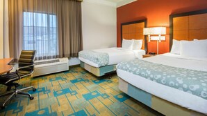Quarto de hotel com duas camas, uma escrivaninha, uma cadeira e uma janela grande com cortinas.