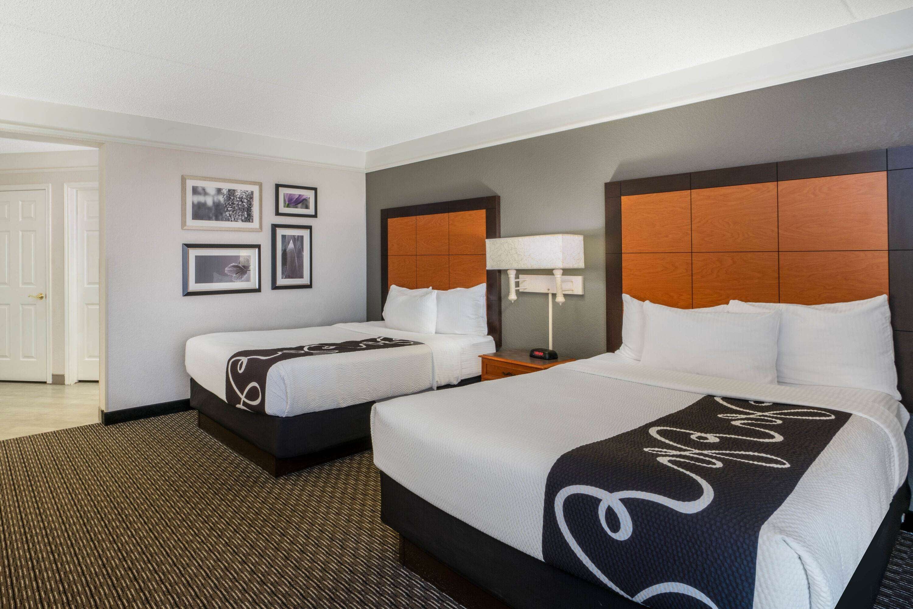A hotel room with two beds, a large window, and a door leading to a hallway.