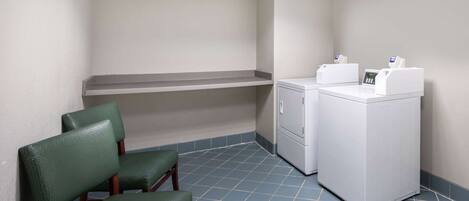 A room with a washing machine, two green chairs, and a shelf.
