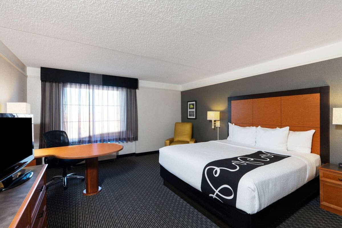 Ett hotellrum med en säng, ett skrivbord, en stol, en tv och ett fönster med gardiner.