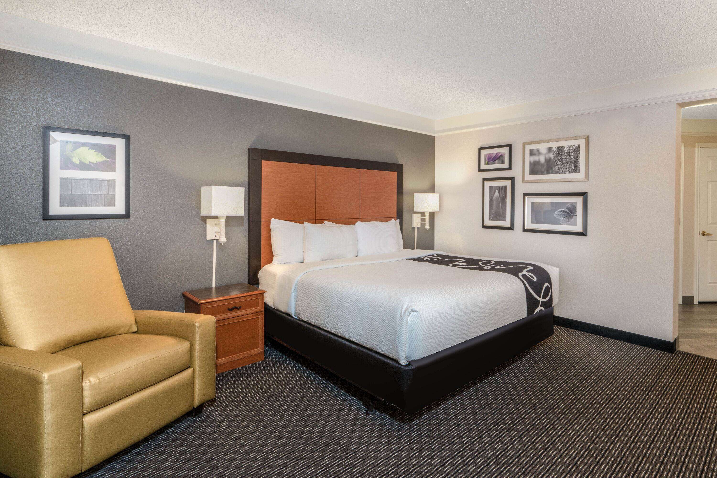 A hotel room with a bed, a chair, a nightstand, and framed pictures on the wall.