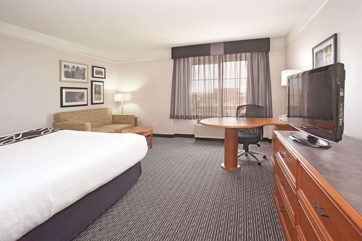 A hotel room with a bed, a sofa, a desk with a chair, a television, and a window with curtains.