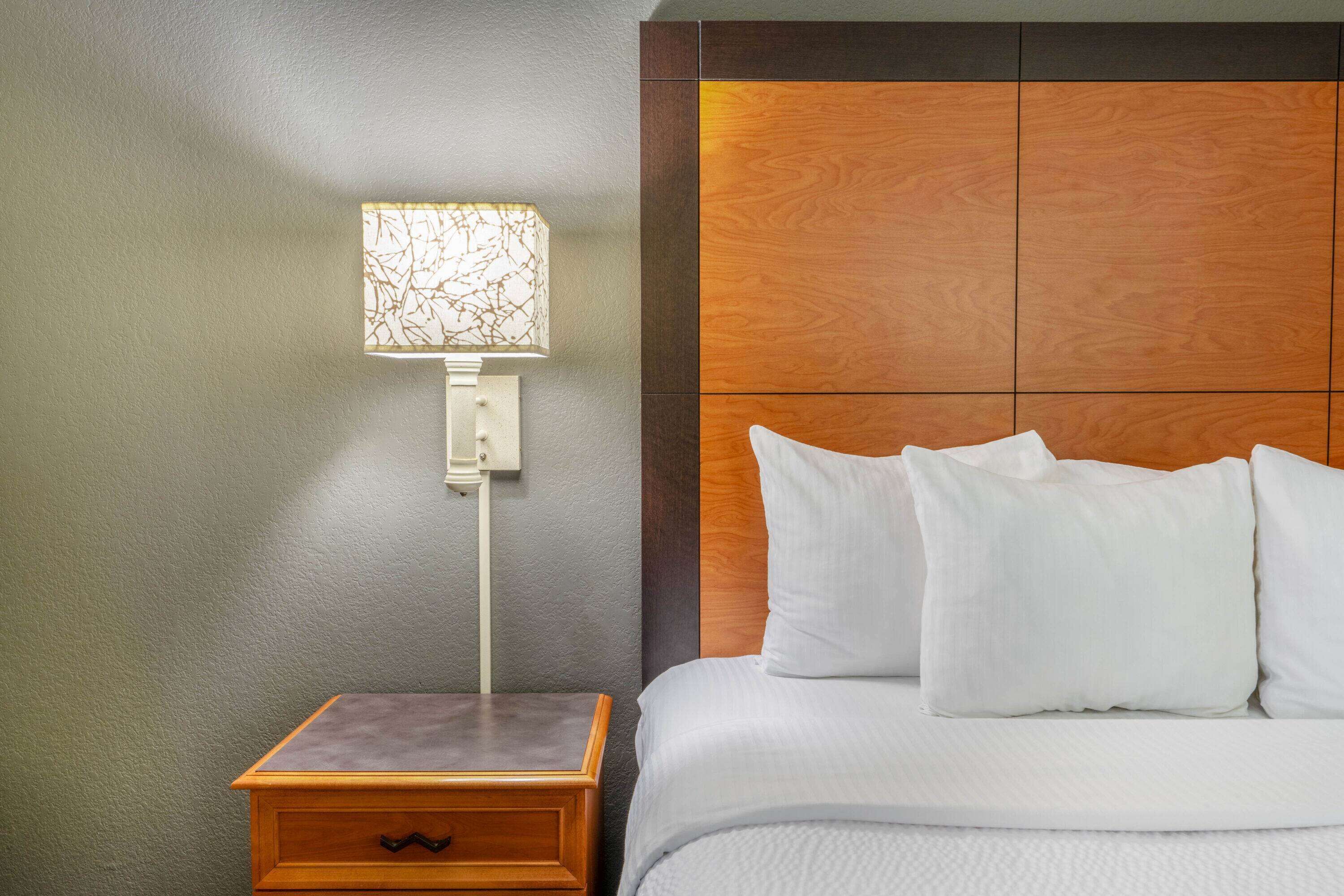 A neatly made bed with white linens and pillows, a bedside table with a lamp, and a wooden headboard.