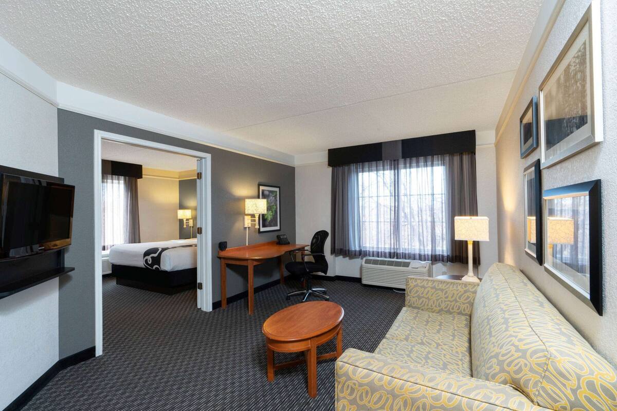A hotel room with a bed, a desk, a chair, a sofa, a TV, and a window with curtains.