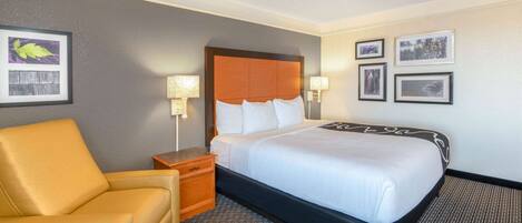 A hotel room with a bed, a chair, a nightstand, and framed pictures on the wall.