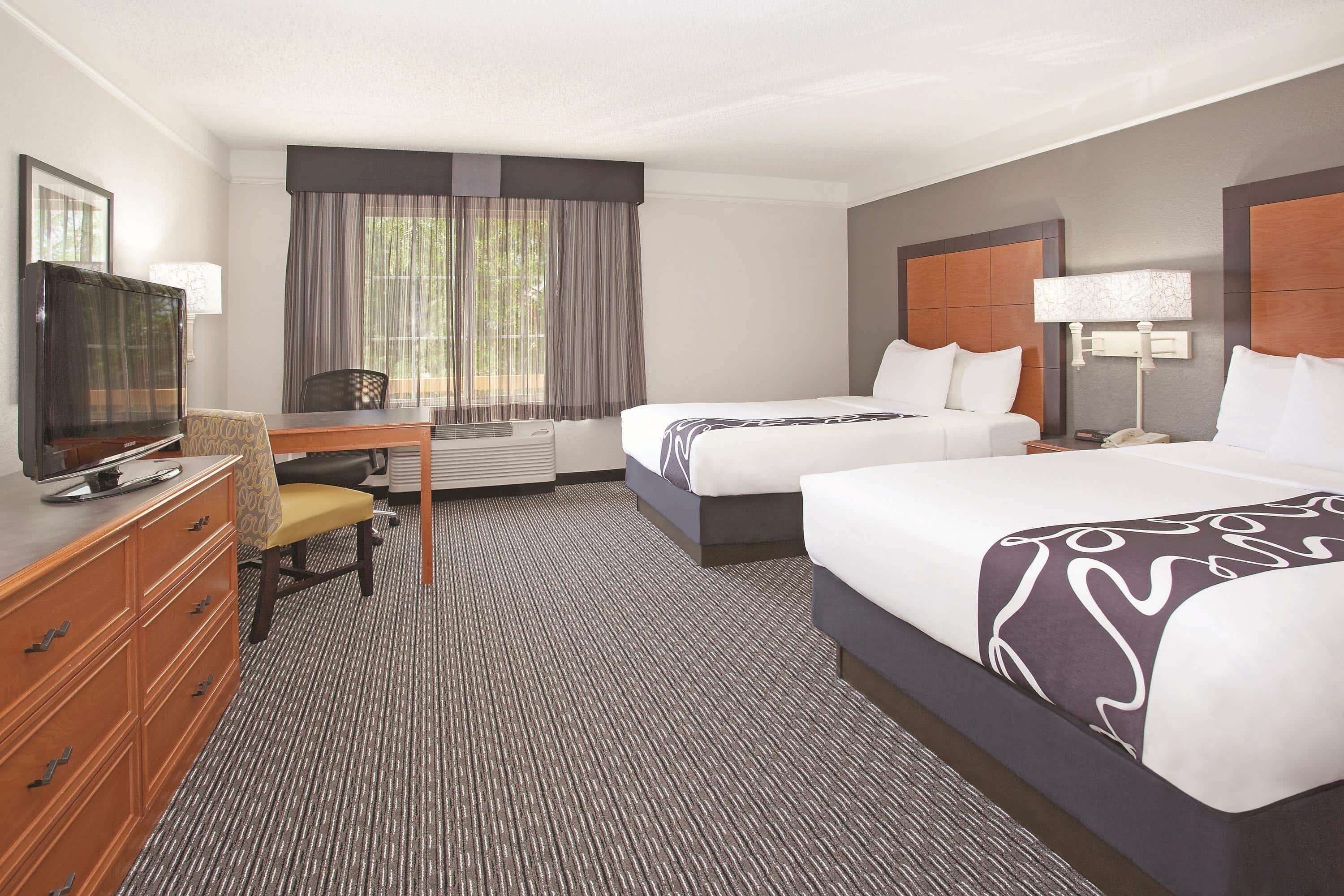 A hotel room with two beds, a desk with a chair, a television, and a dresser.