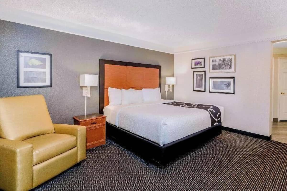A hotel room with a bed, a chair, a nightstand, and wall-mounted lamps.