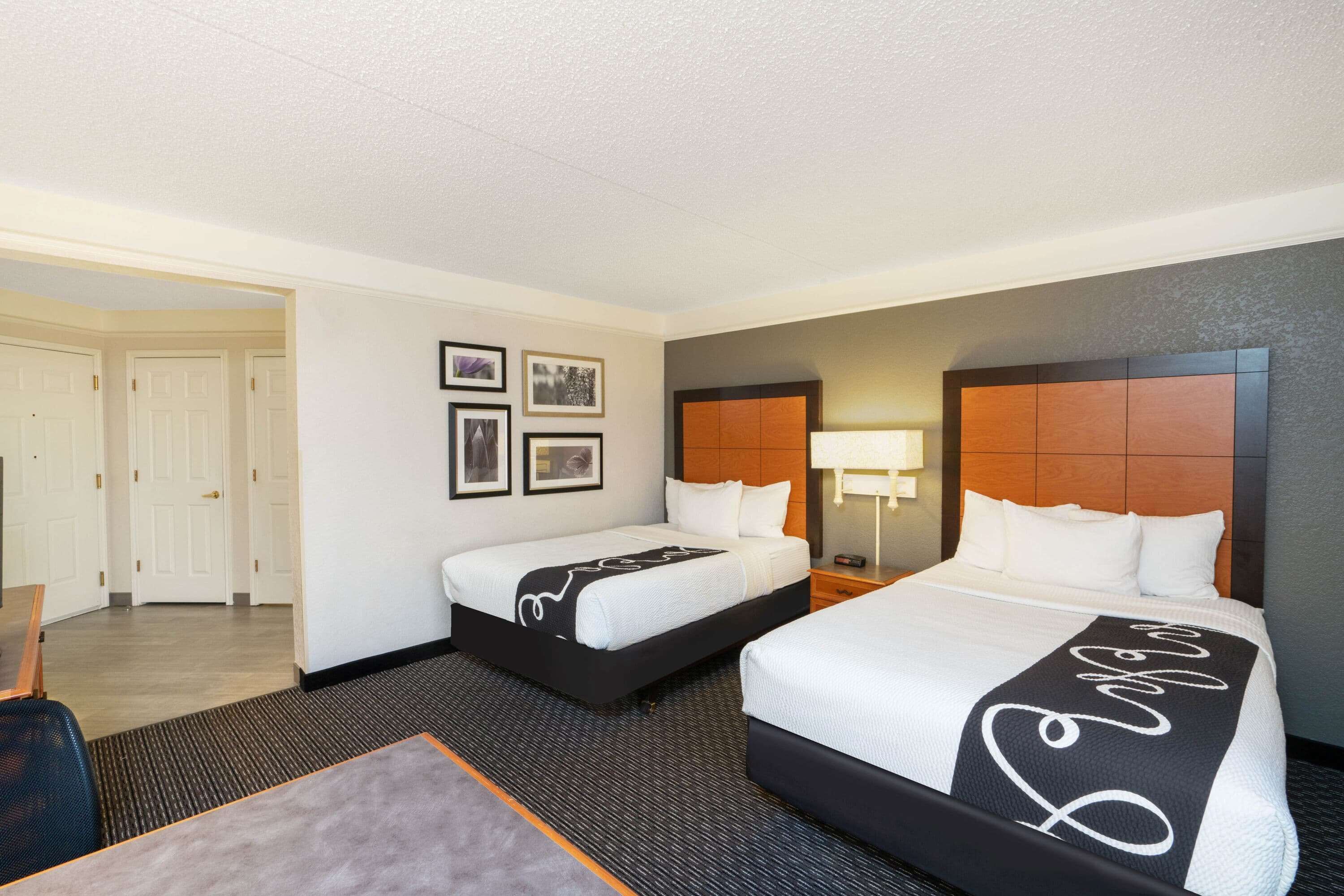 Een hotelkamer met twee bedden, een bureau en een stoel. Er hangen prestaties aan de muur en op het nachtkastje staat een lamp.