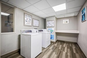 A laundry room with two washing machines, a dryer, and a shelf with hanging clothes.