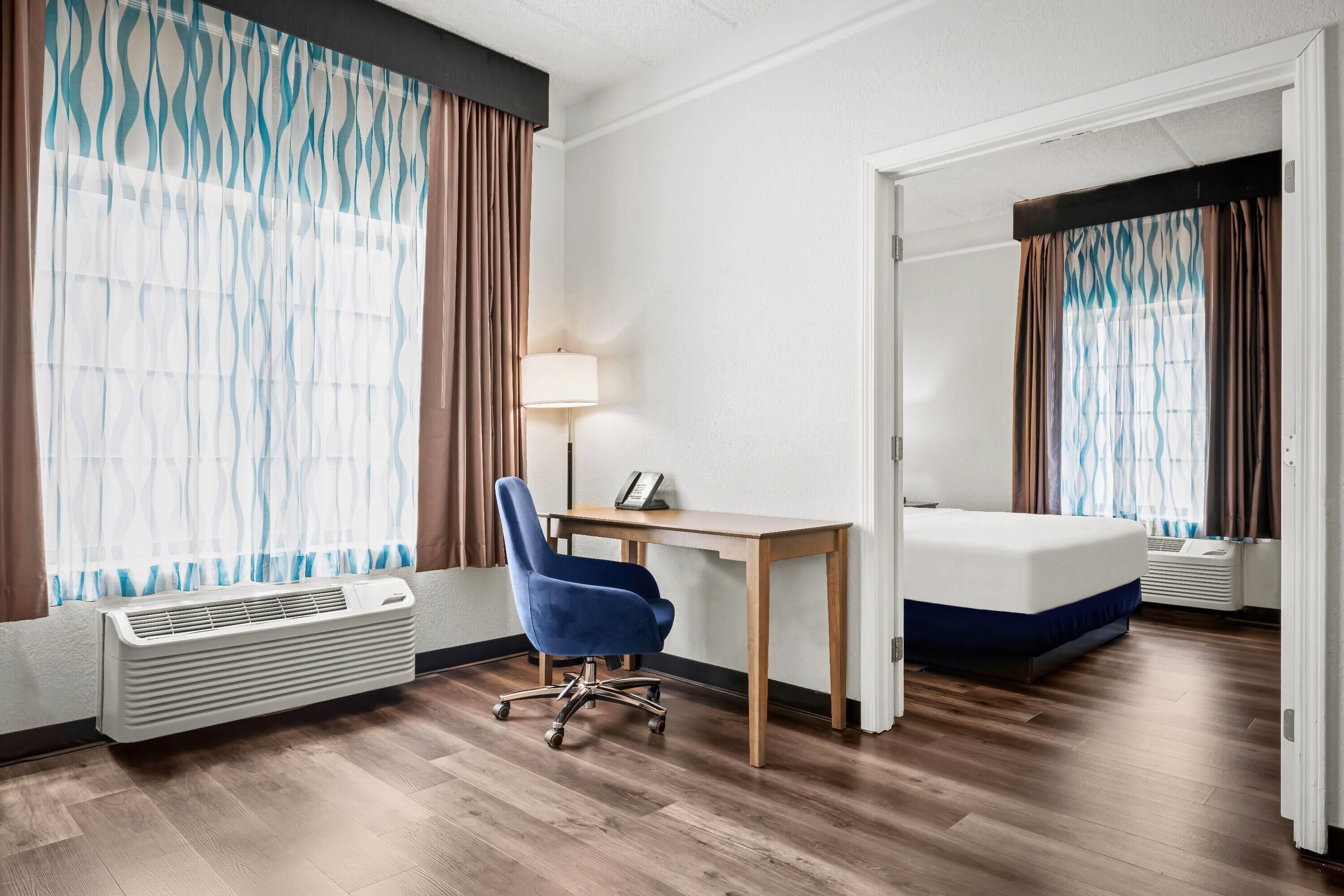 A hotel room with a bed, desk, chair, and air conditioning unit.