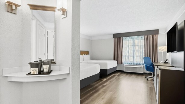 Une chambre d’hôtel avec un lit, un bureau et une chaise, une télévision et une fenêtre avec des rideaux.