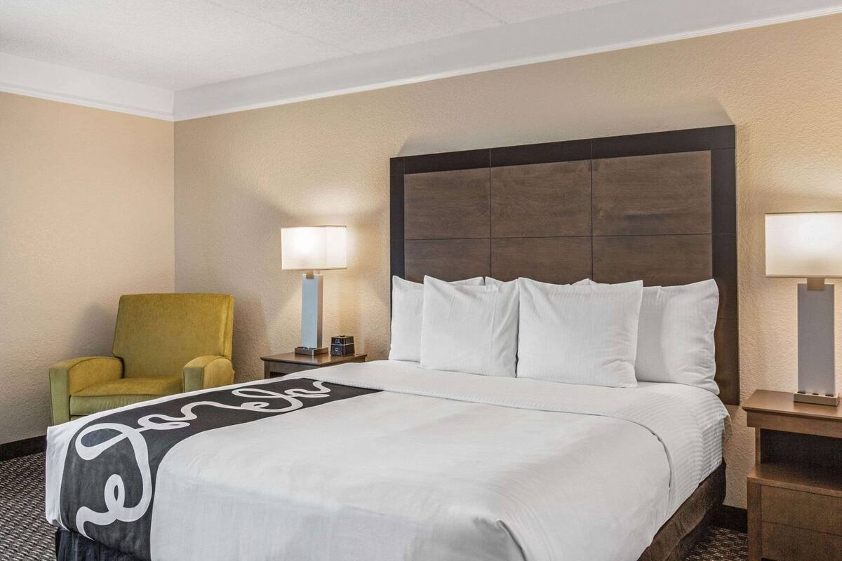 Ein Hotelzimmer mit einem großen Bett, einem gelben Sessel, zwei Nachttischlampen und einem Kopfteil.