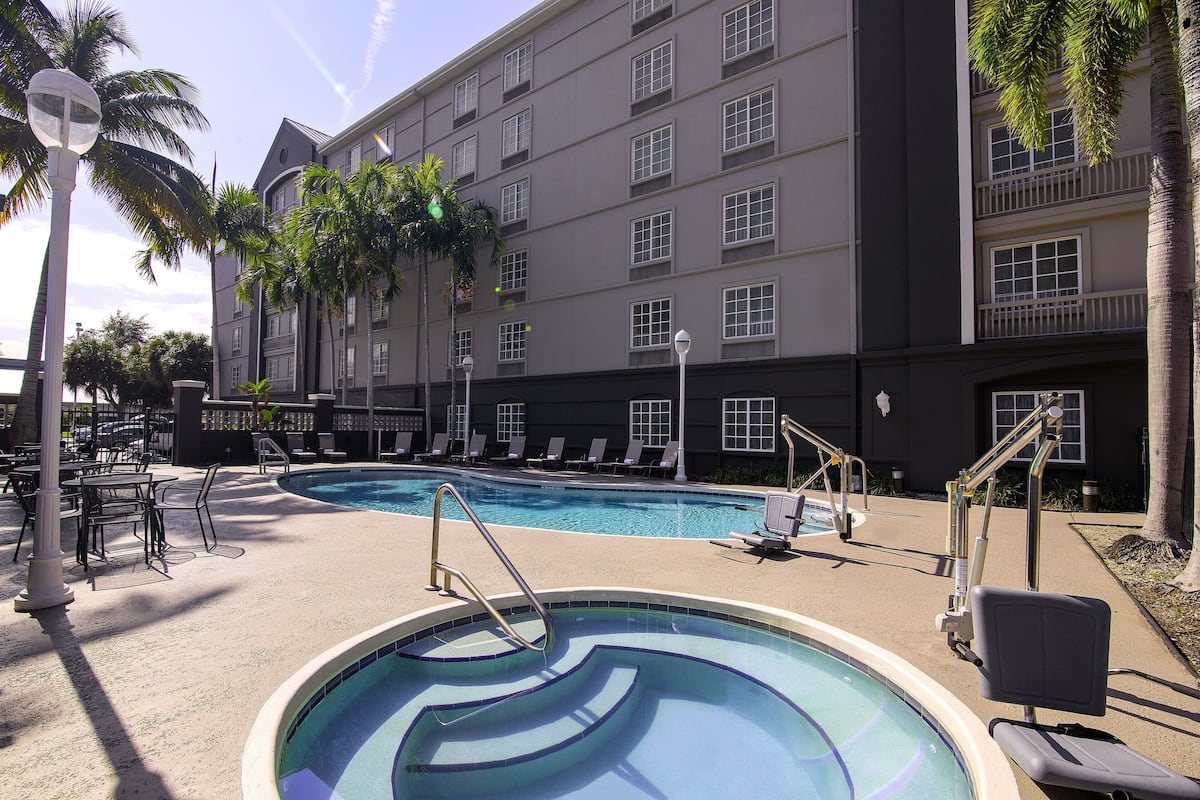 Ein Hotelpoolbereich mit Liegestühlen, einem Pool mit wellenförmigem Design und einem Gebäude mit mehreren Fenstern und Balkonen.