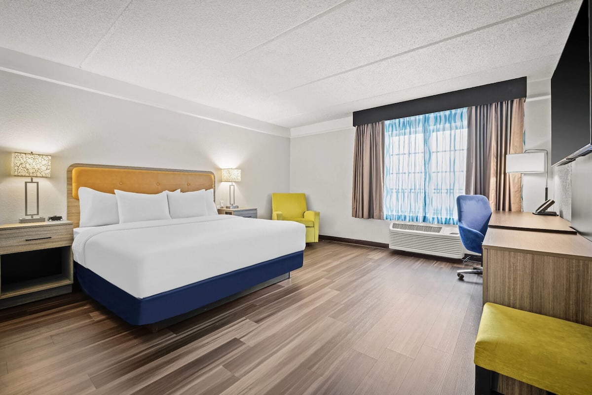 Ein Hotelzimmer mit einem großen Bett, einem Schreibtisch, einem Stuhl und einem Fenster mit Vorhängen.