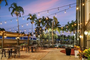 An outdoor patio area with string lights, palm trees, and outdoor seating.
