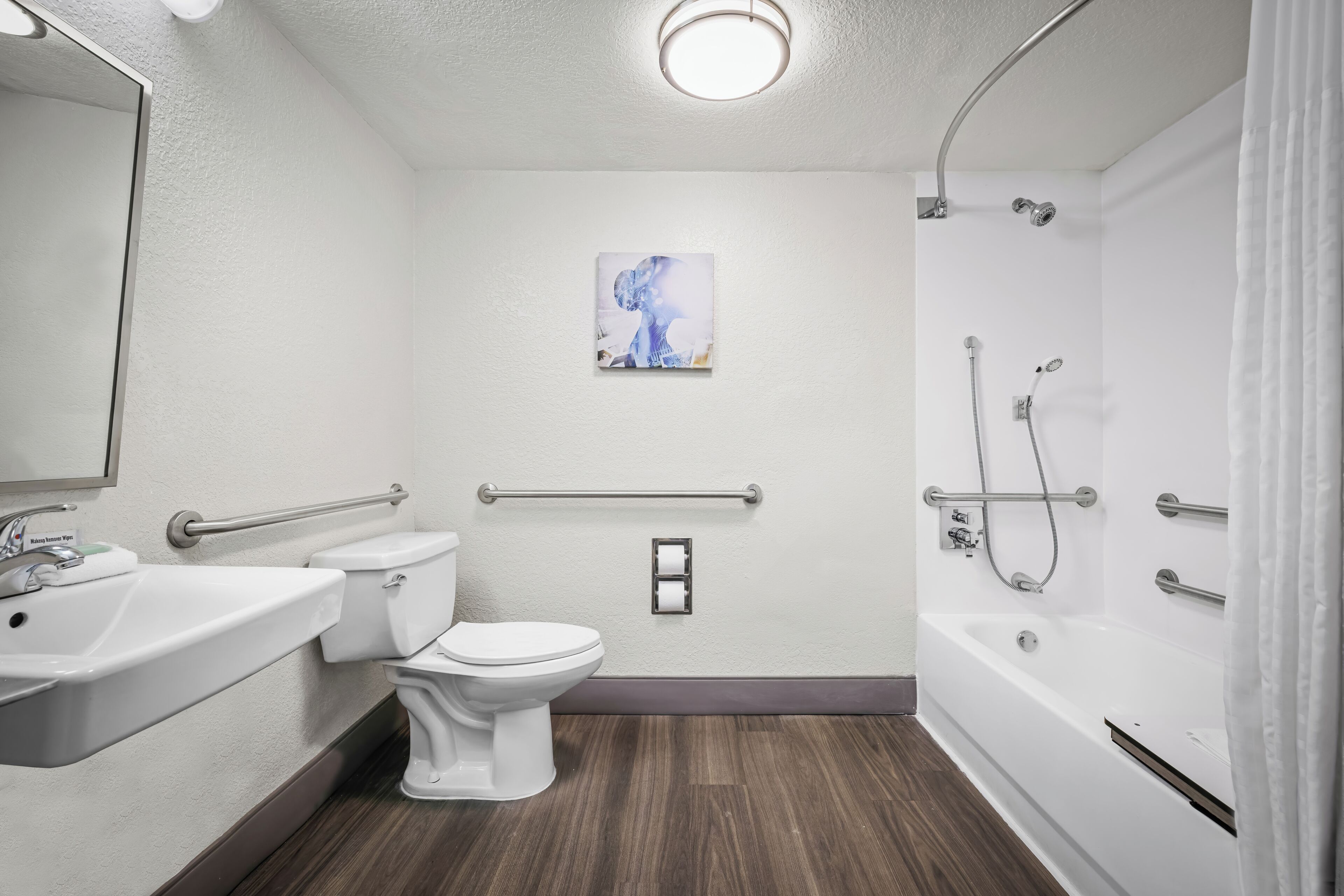 A bathroom with a toilet, sink, shower, and grab bars.