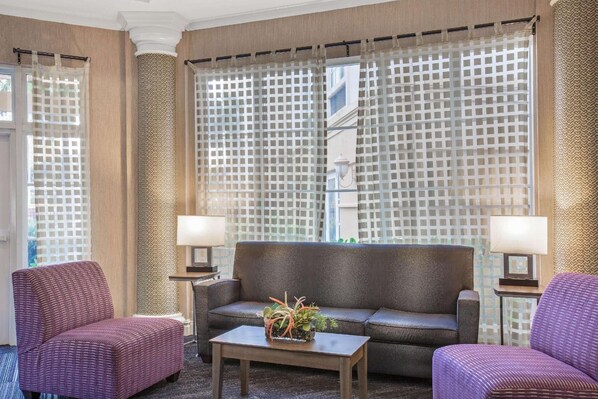A hotel lobby with a sofa, two armchairs, a coffee table, and patterned curtains.