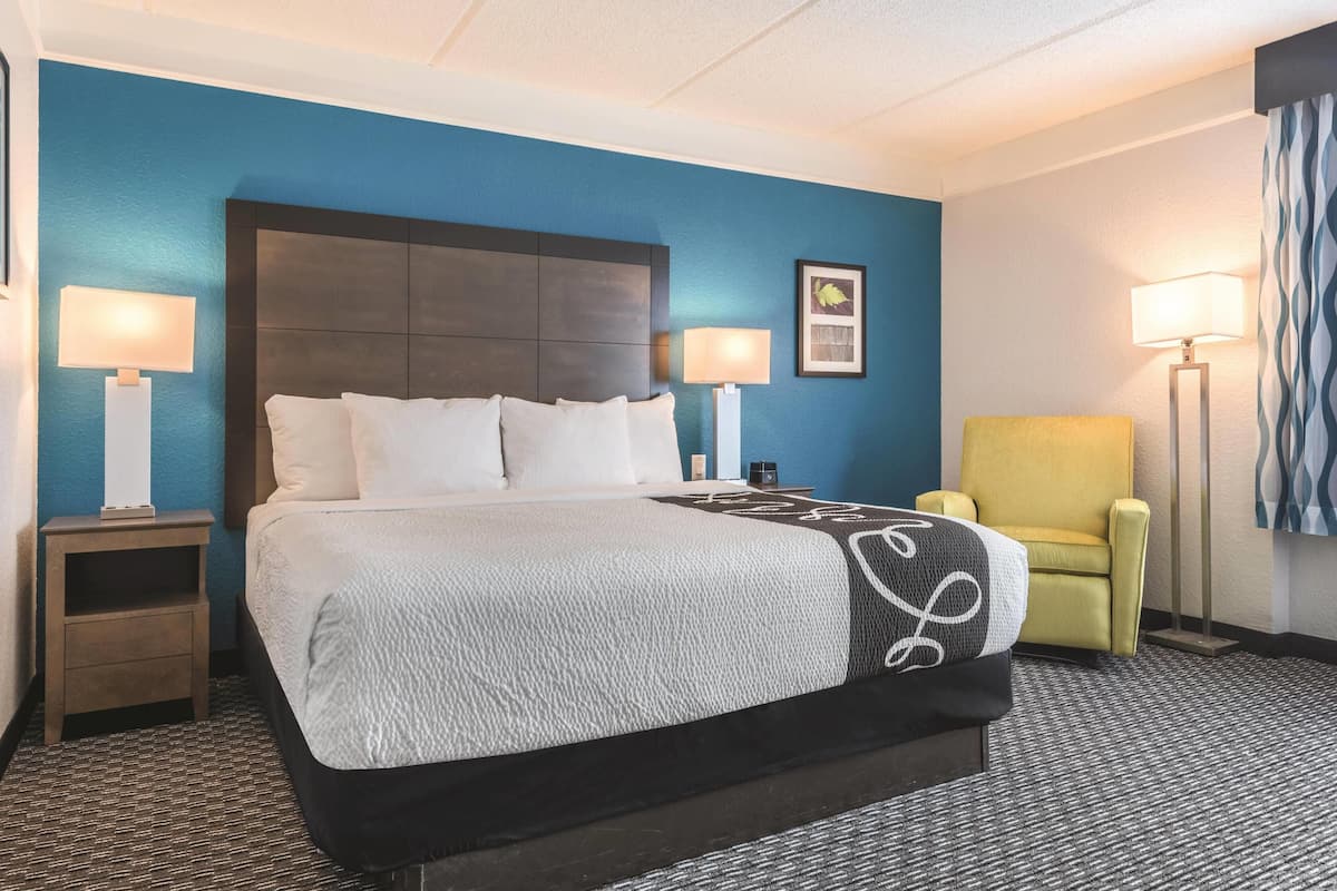 Ein Hotelzimmer mit einem großen Bett, zwei Nachttischen, einem Sessel und einem Beistelltisch.