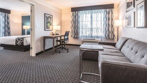 A hotel room with a bed, a desk, a chair, a sofa, and a large window with curtains.