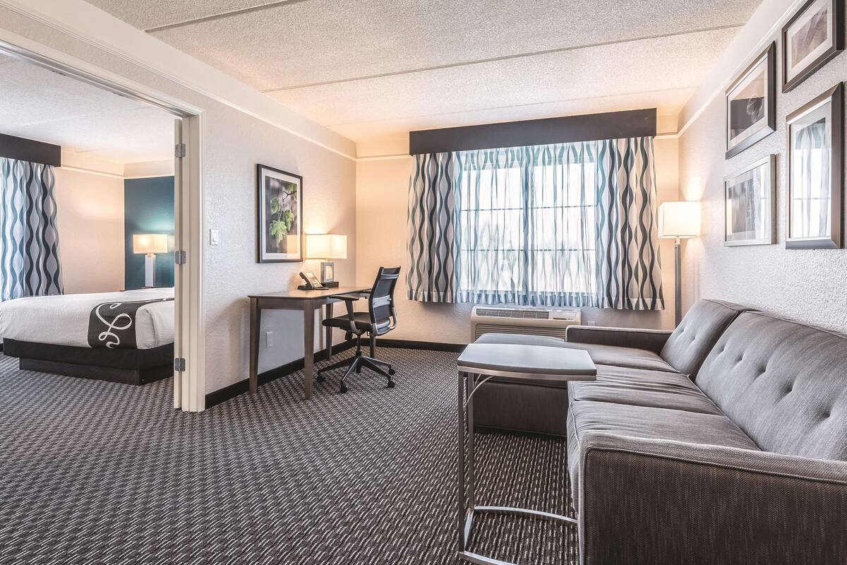 Ein Hotelzimmer mit Bett, Schreibtisch, Sessel, Sofa und einem großen Fenster mit Vorhängen.