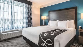 Une chambre d’hôtel avec un grand lit, une table de chevet avec une lampe, une fenêtre avec des rideaux à motifs et un radiateur mural.