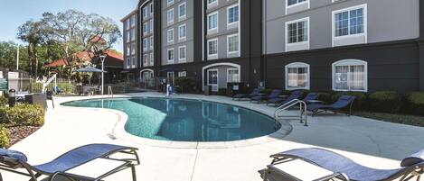 A hotel with a swimming pool, lounge chairs, and a fenced patio area.