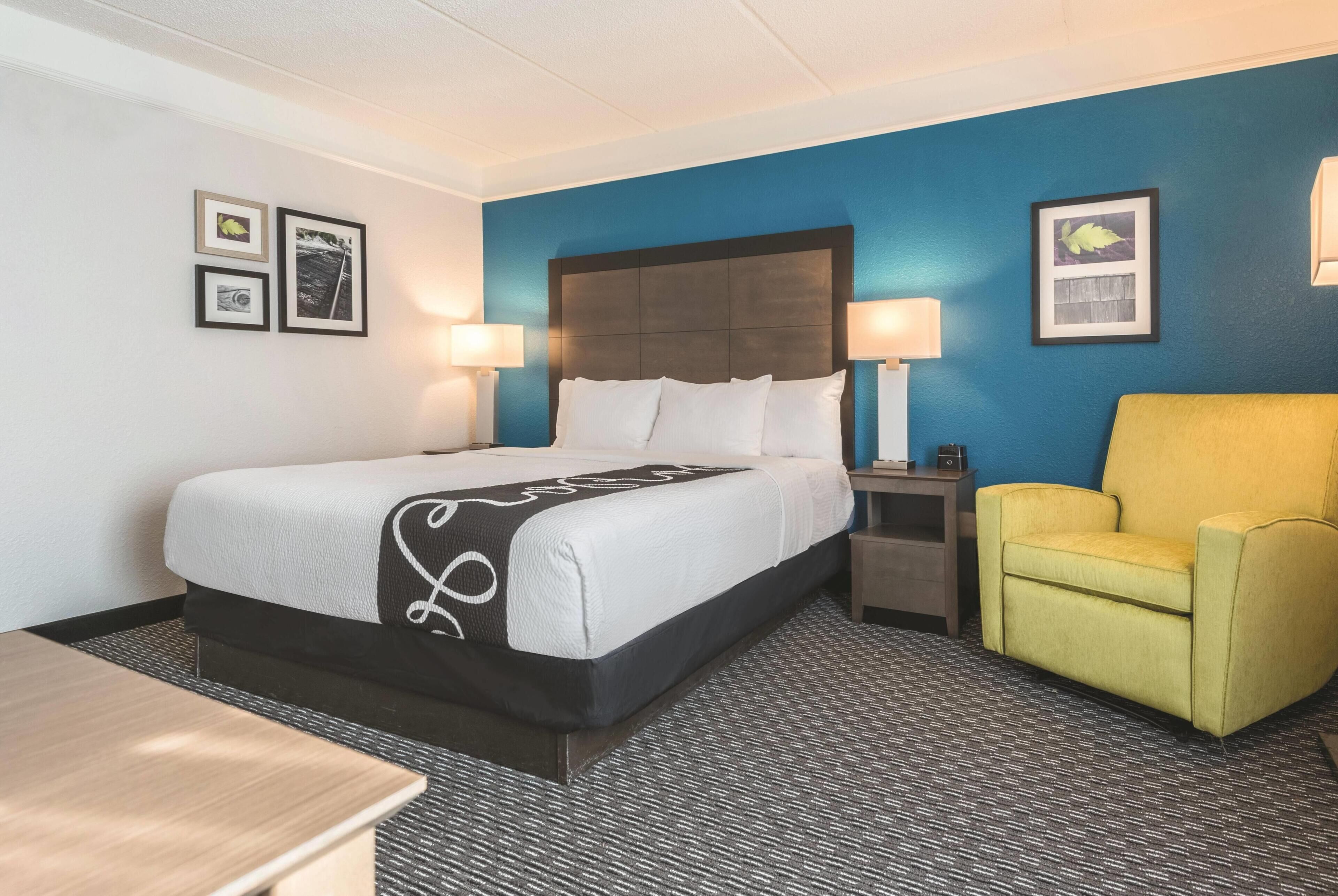 Una habitación de hotel con cama, sillón, mesita de noche y decoración en la pared.