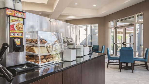A breakfast bar with a coffee machine, a waffle display, and a glass display case with pastries.