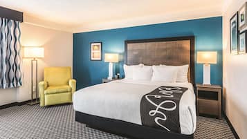 Una habitación de hotel con una cama grande, dos mesitas de noche, una silla y una alfombra estampada.