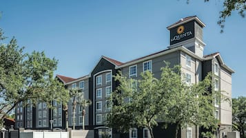 Een meerhoog hotel met een opvallend 'La Quinta'-bord op het dak, omgeven door bomen en een verzorgd gazon.