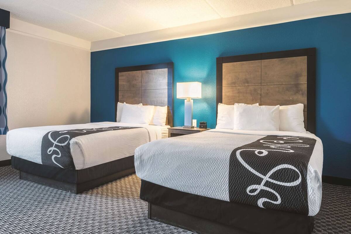 Ein Hotelzimmer mit zwei Betten, einem Nachttisch mit Lampe und einer blauen Akzentwand.