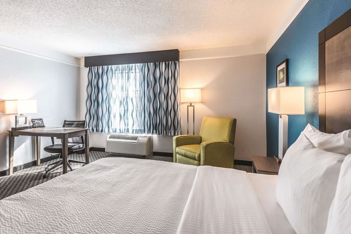 Ein Hotelzimmer mit Bett, Schreibtisch mit Stuhl, Stehlampe und einem an der Wand befestigten Fernseher.