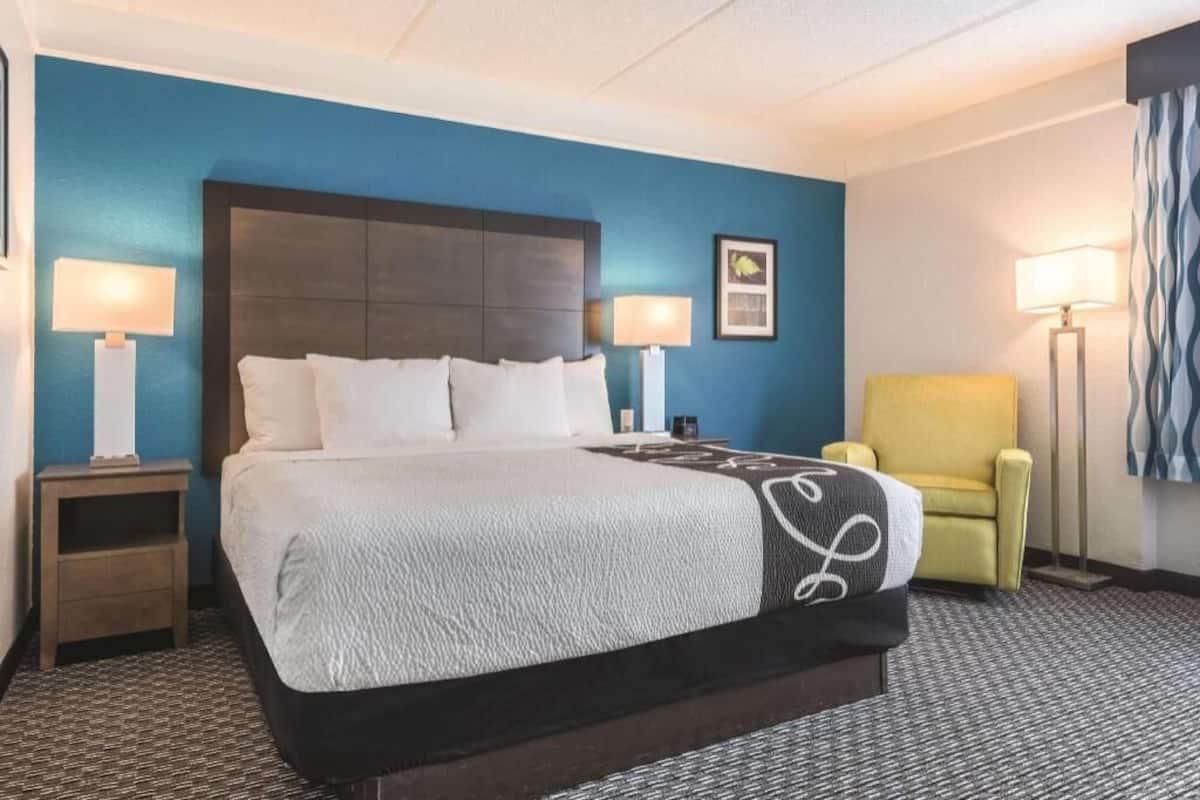 Ein Hotelzimmer mit einem großen Bett, zwei Nachttischen, einem Sessel und einer Lampe.