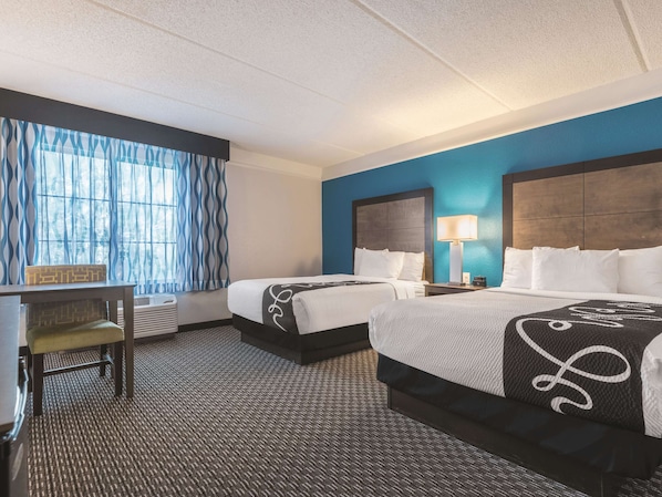A hotel room with two beds, a desk, and a chair.