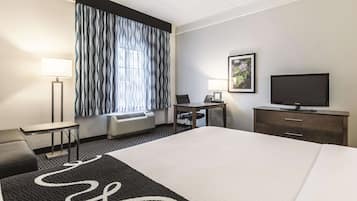 Una habitación de hotel con una cama grande, un escritorio, una silla, un televisor y una ventana con cortinas.