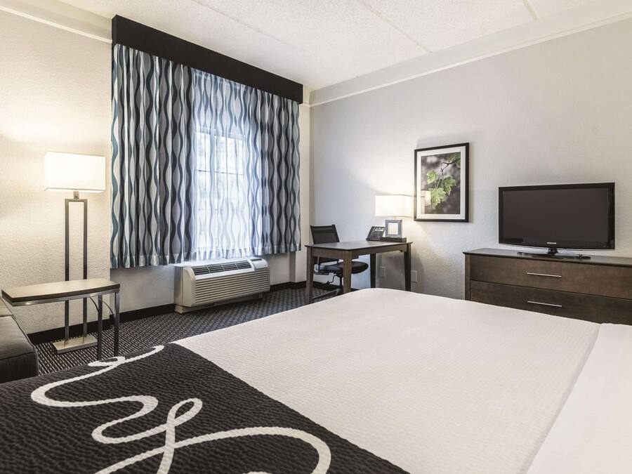 A hotel room with a large bed, a desk, a chair, a television, and a window with curtains.