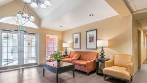 Un hall con sofá, sillón y mesa de centro, una araña, cuadros enmarcados en la pared y una señal de salida.