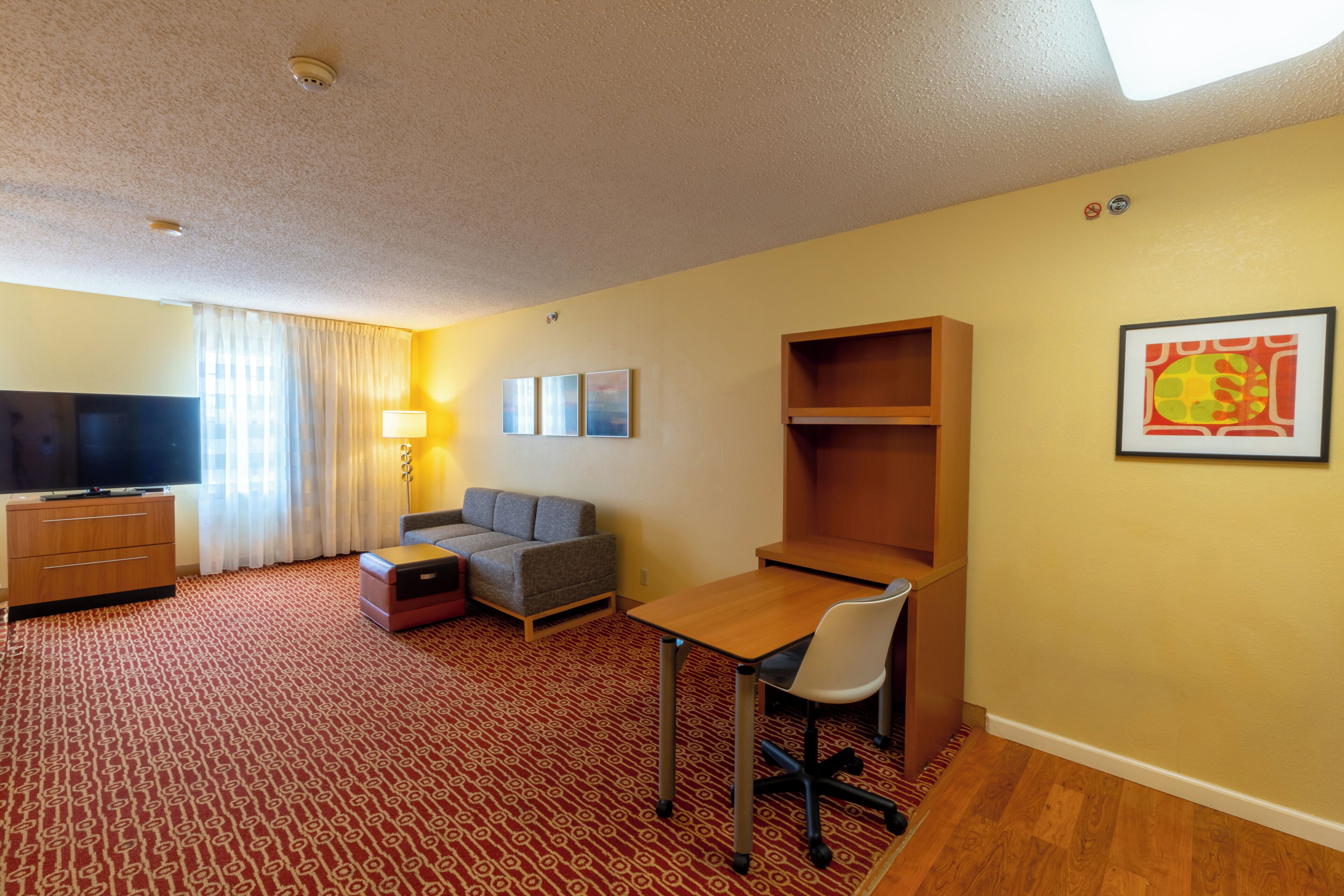 Ein Hotelzimmer mit Fernseher, Sofa, Schreibtisch, Stuhl und einem Holzboden.