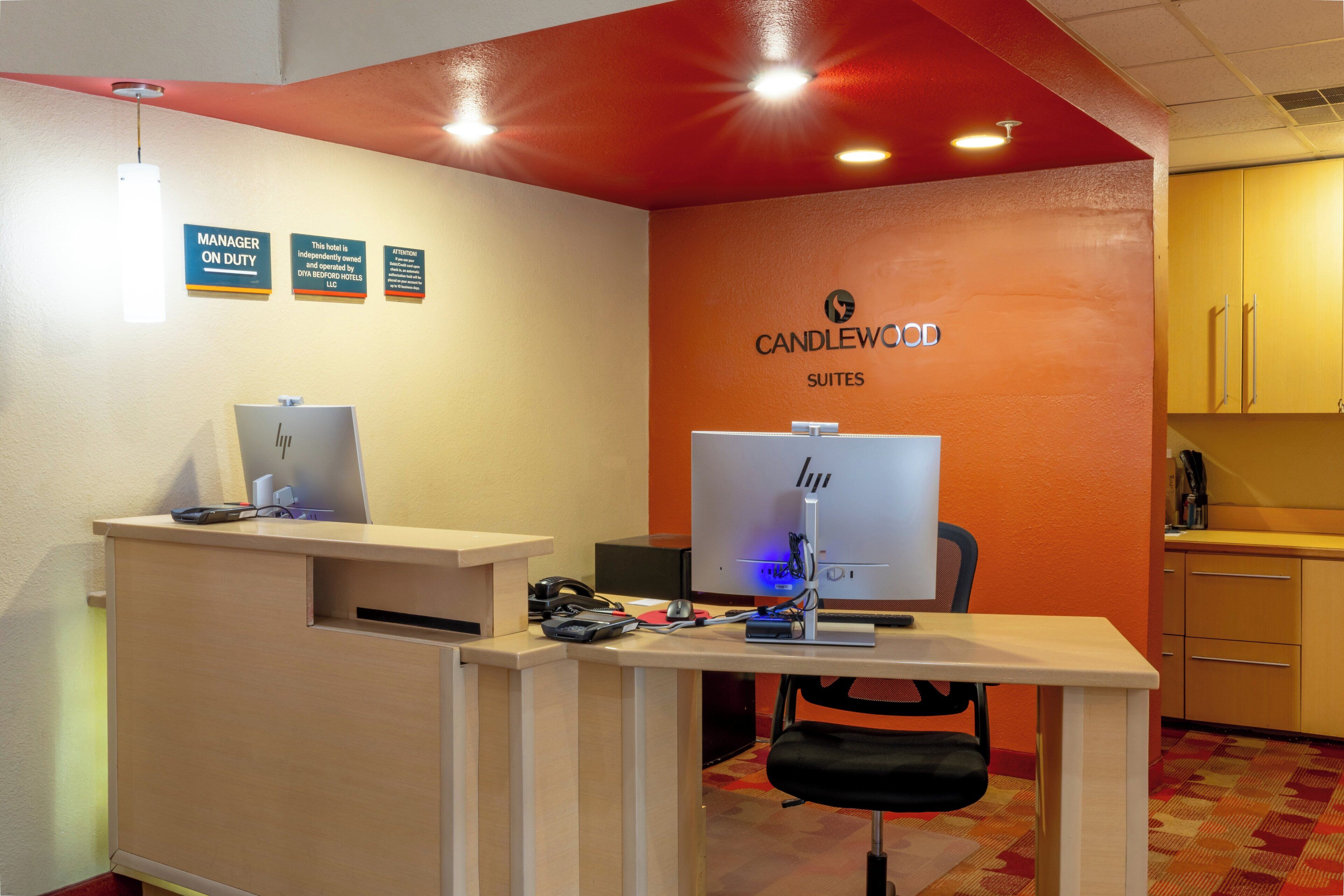 A reception desk with computers, a black office chair, and a wall with a 'CANDLEWOOD SUITES' sign.