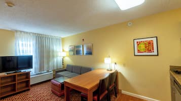 Habitación de hotel con televisor de pantalla plana, sofá, mesa de comedor, lámpara y un cuadro en la pared.