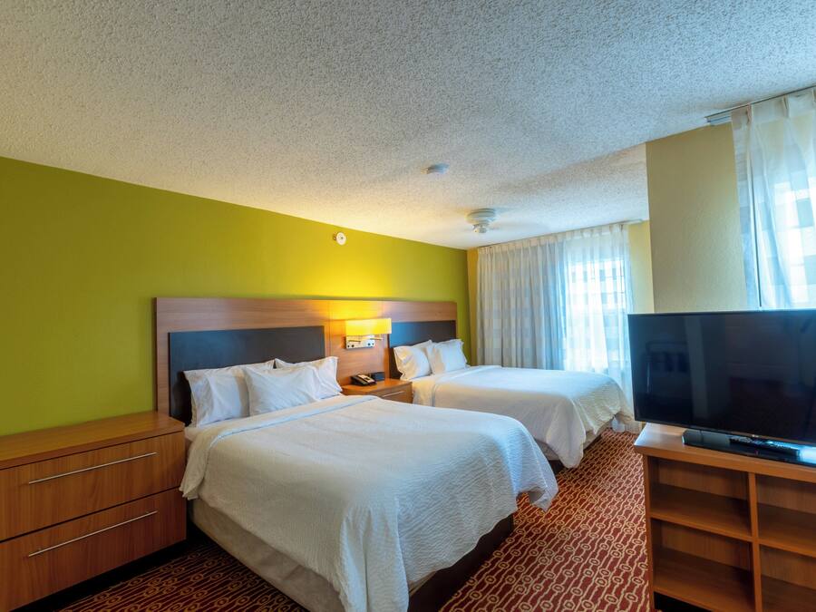 A hotel room with two beds, a TV, a desk, and a lamp.