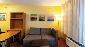 Una habitación de hotel con sofá, una mesa, una lámpara y tres cuadros colgados en la pared.