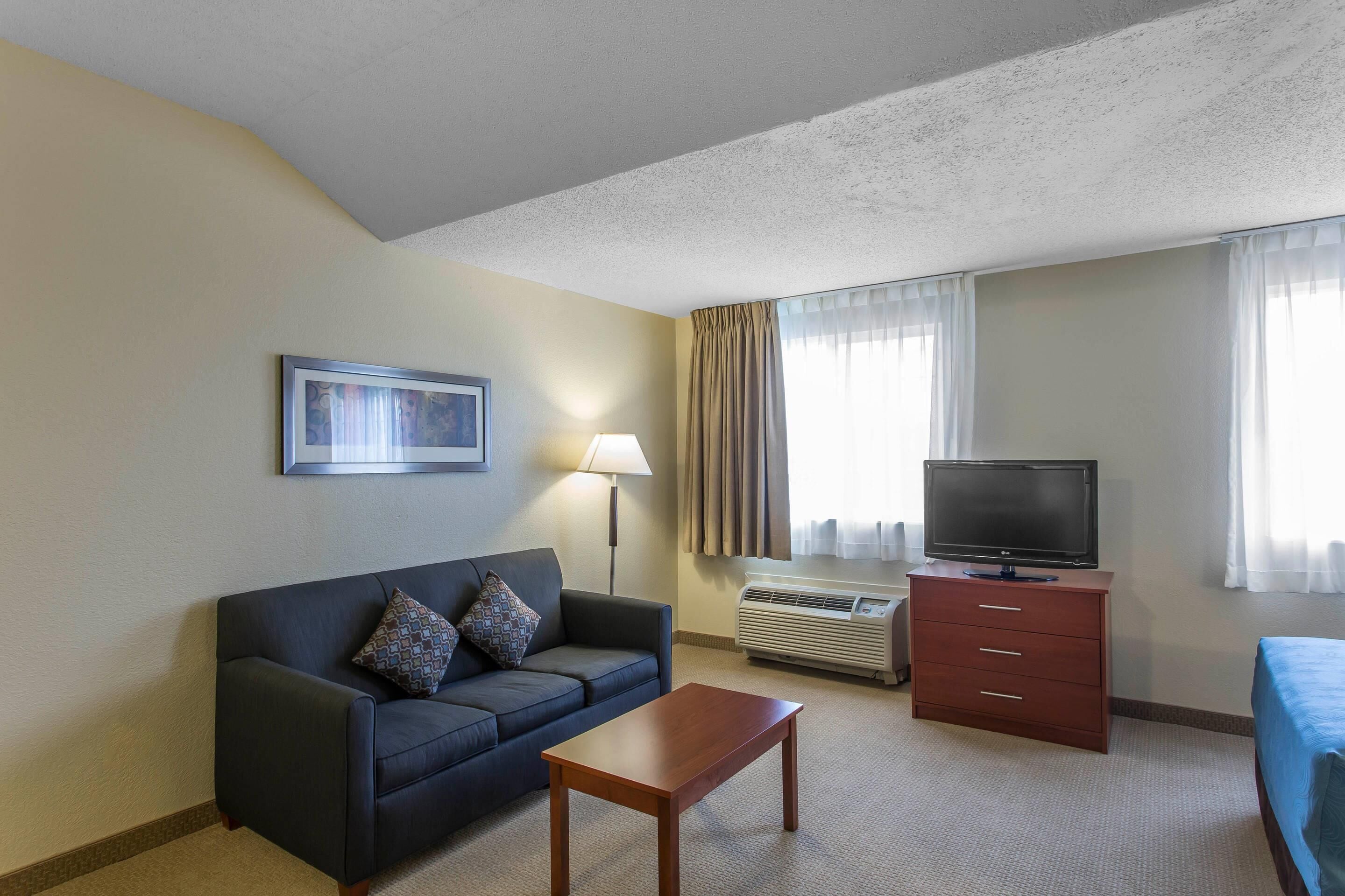 A hotel room with a sofa, a TV on a stand, a small table, and a bed.