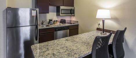 A compact kitchen with a refrigerator, microwave, dishwasher, and a dining table with chairs.