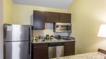 A compact kitchen with a stainless steel refrigerator, microwave, dishwasher, and granite countertop.