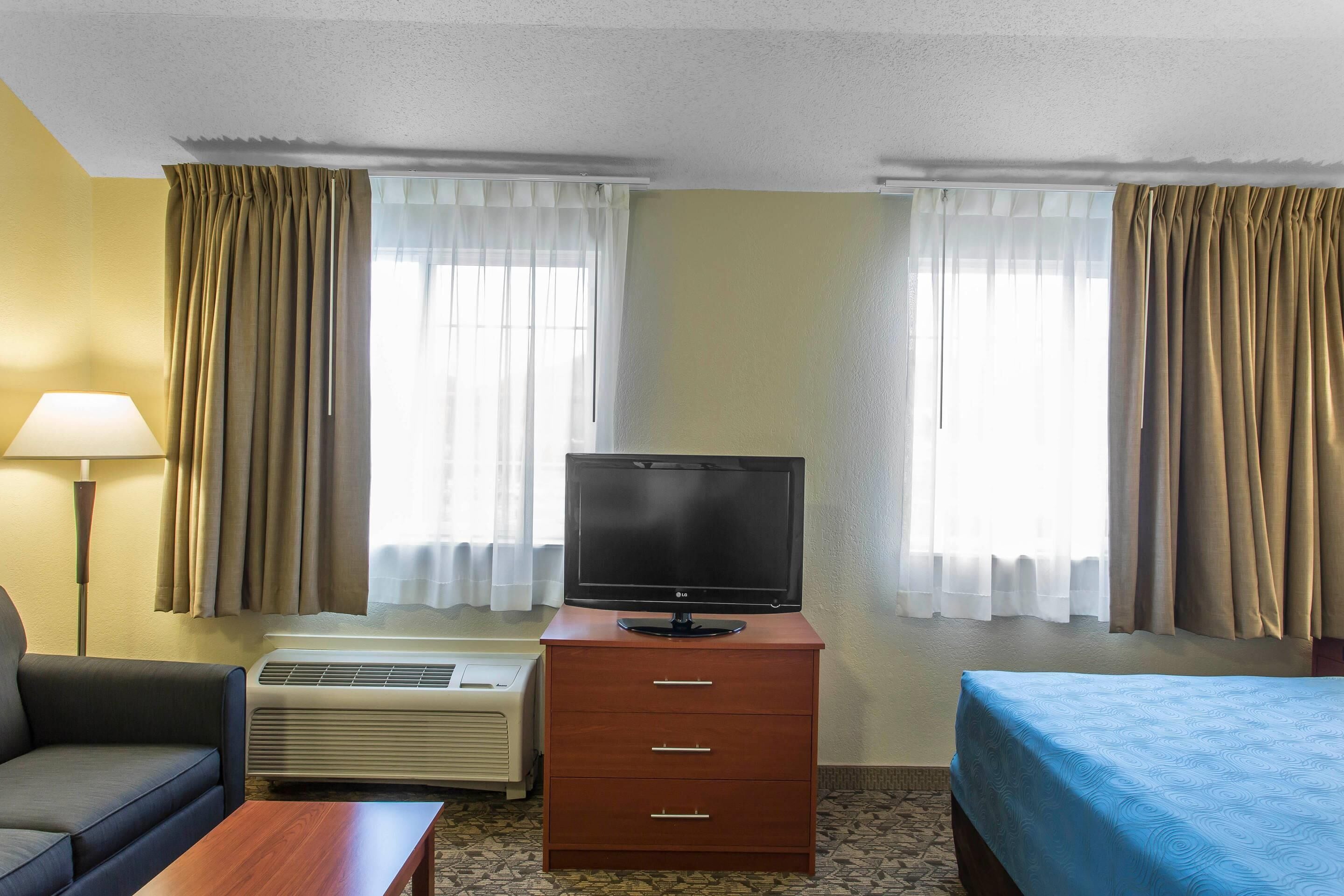 Ein Hotelzimmer mit einem Bett, einem Fernseher auf einer Holzkombie, einem Sofa und einer Klimaanlage.
