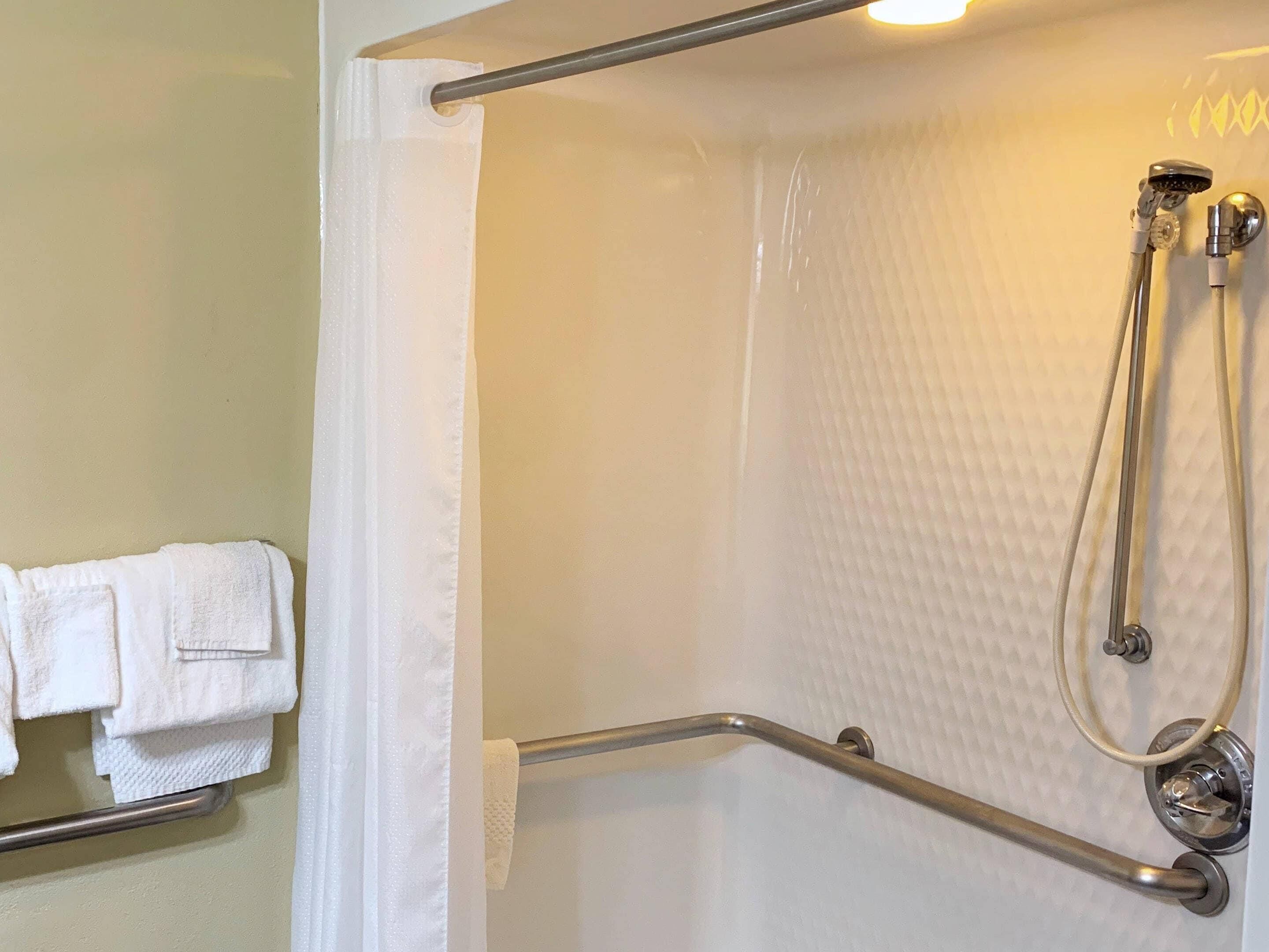 A shower area with a handrail, a showerhead, and a towel rack with folded towels.