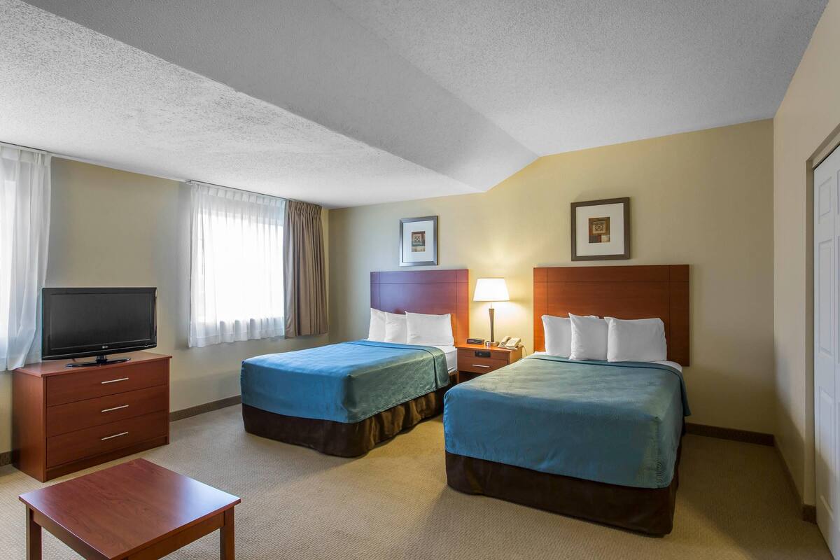 Habitación de hotel con dos camas, televisión, escritorio y lámpara.
