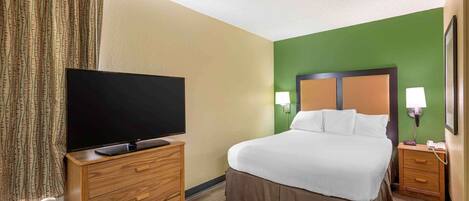 A hotel room with a bed, a television on a wooden dresser, a nightstand with a lamp, and a green accent wall.