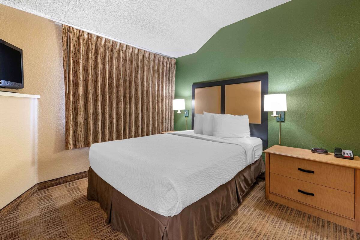 Ein Hotelzimmer mit Bett, Nachttisch, Lampe, Fernseher und Vorhang.